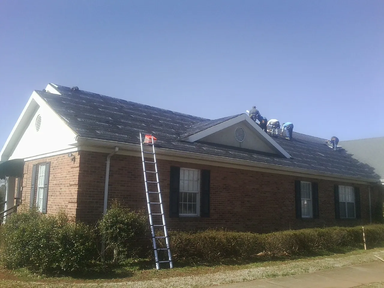 Crew tearing shingles off a brick ranch roof with a ladder set — Metal Roof Repair work by our crew in Morganfield