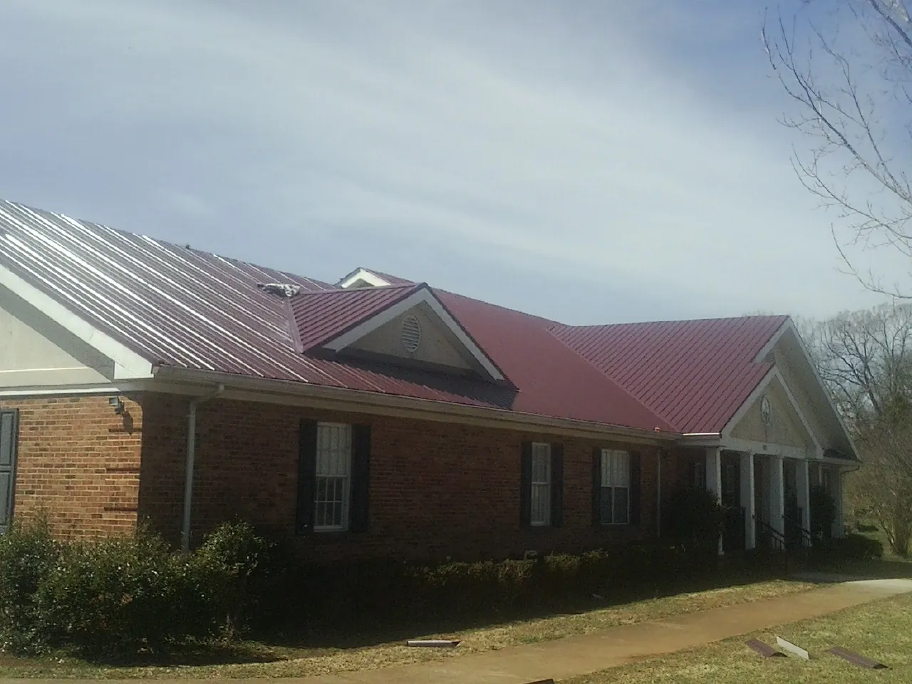 Red metal roof with gabled entries on a long brick building, from a Hail Damage Roof Repair job in Morganfield