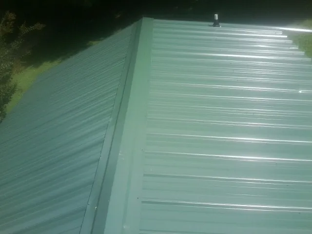 New green metal panels meeting at the ridge of a roof — Flat Roof Repair work by our crew in Morganfield