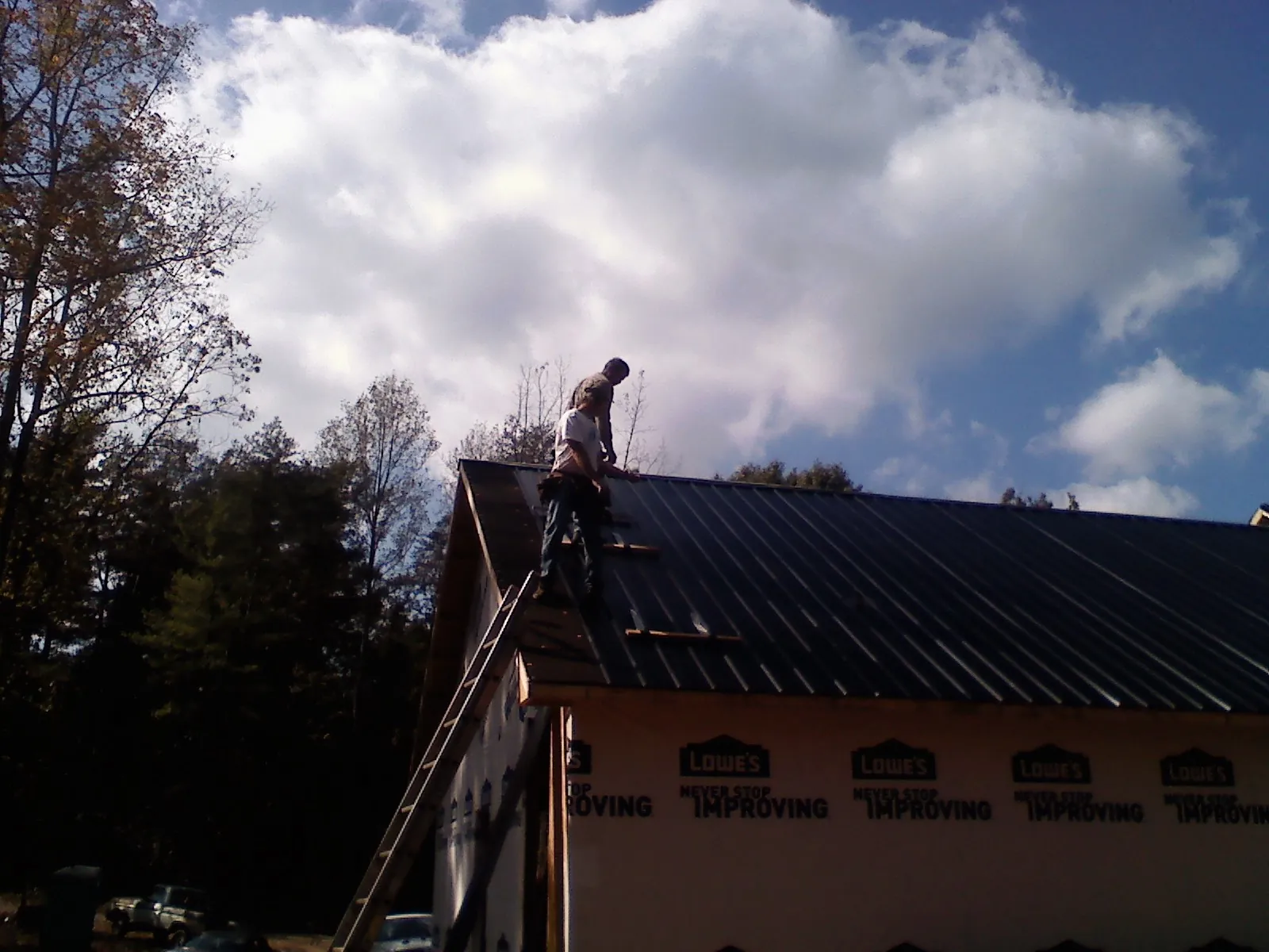 Roofer fastening dark metal panels high against a cloudy sky, from a Roof Inspection job in Morganfield
