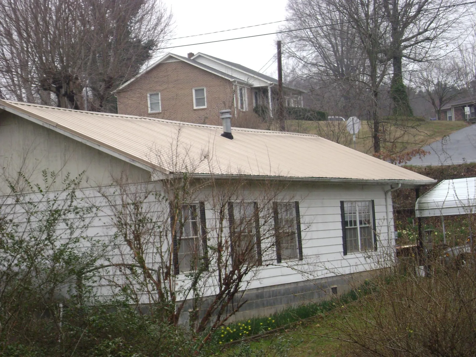 Tan metal roof on a white sided house set into a hillside — Commercial Roofing by Roofing Brothers in Morganfield